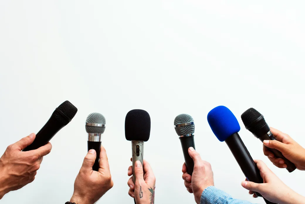 Several hands holding microphones at a press conference